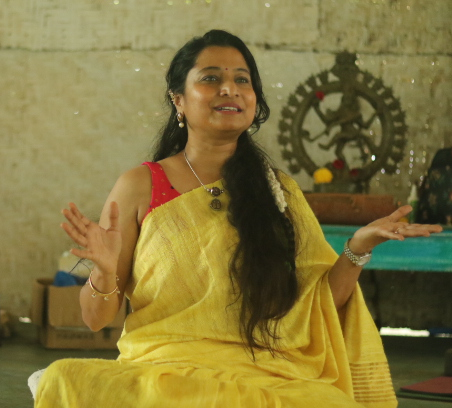 Neha in a yellow sari, speaking warmly during a session